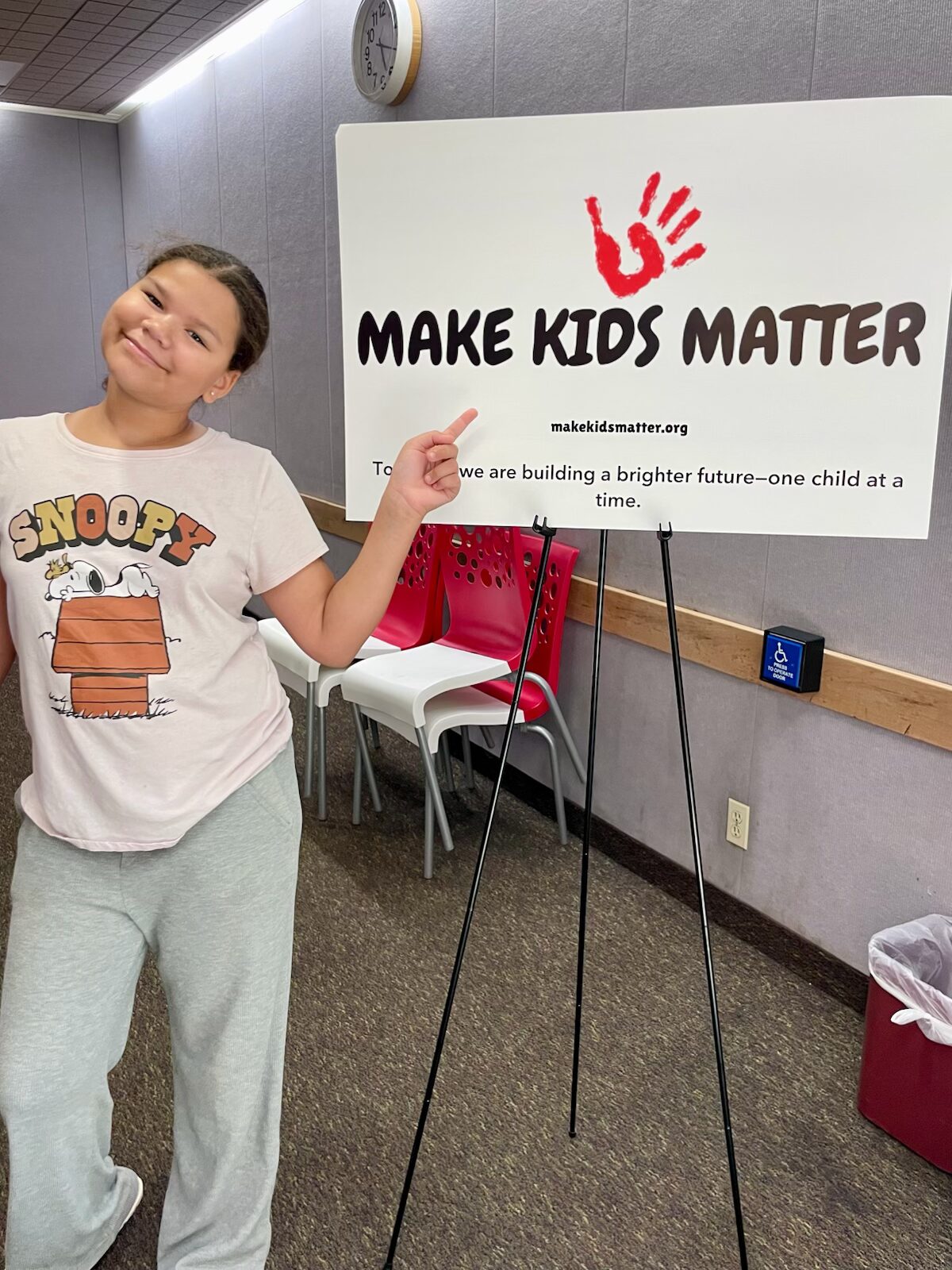 A young girl pointing at the Make Kids Matter sign